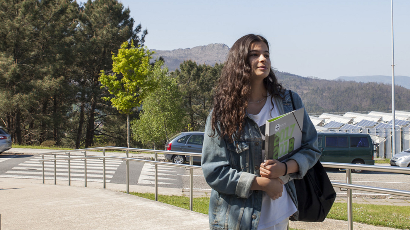 Estudiante con una carpeta dirigiéndose a un edificio en el campus de Vigo