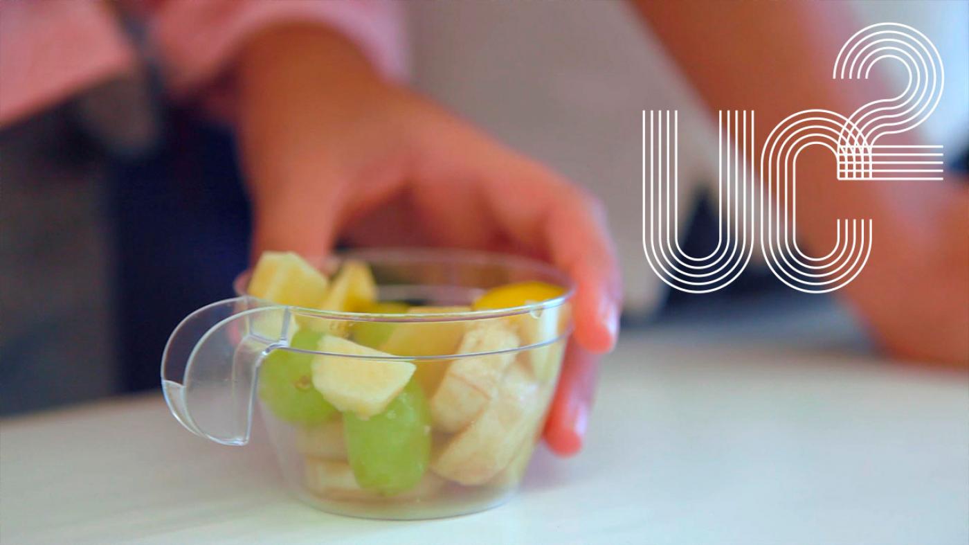 Imaxe dunha man que agarra unha taza transparente con froita
